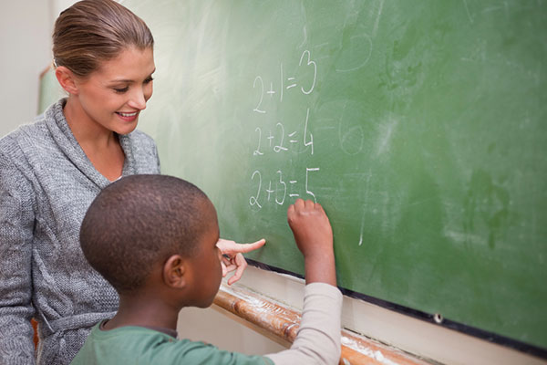 A woman teaching a boy math while he is writing on a green chalkboard