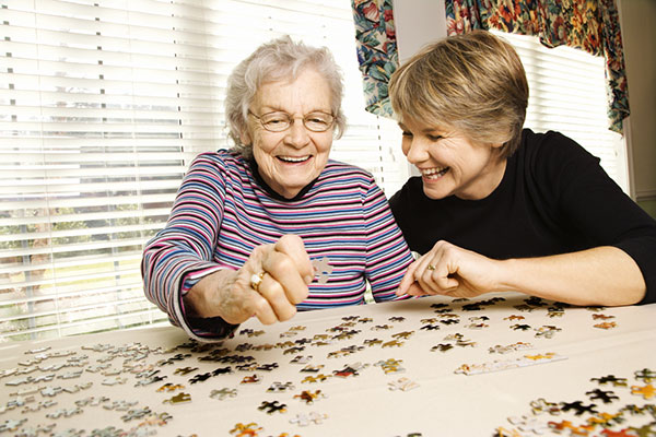 A middle-aged woman helping an elderly woman with a puzzle on a table
